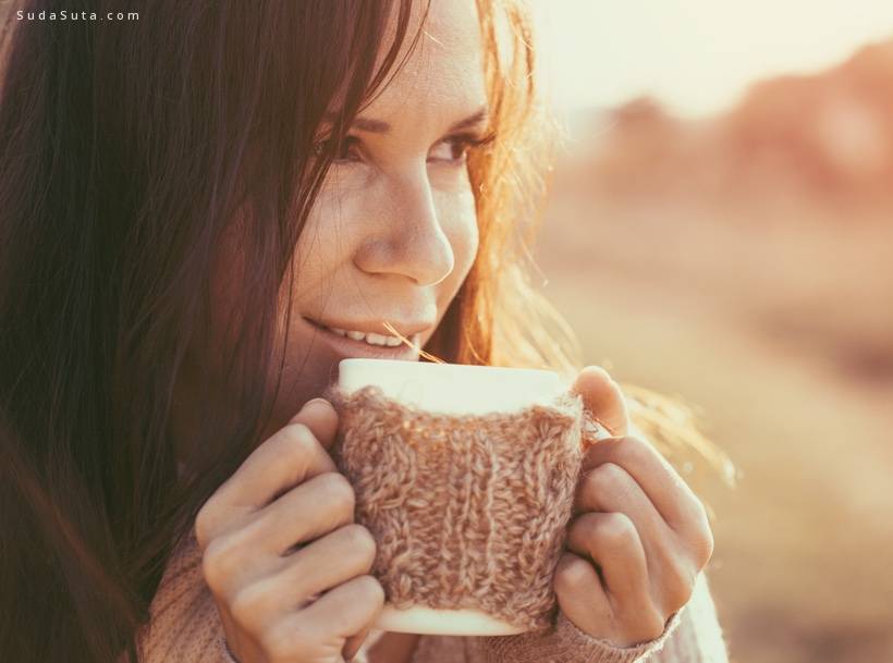 Woman wearing warm knit clothes drinking cup of hot tea or coffee outdoors in sunlight